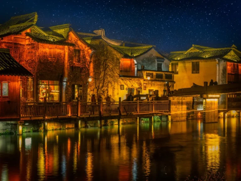 Puente de madera sobre un río de noche iluminado por un farol